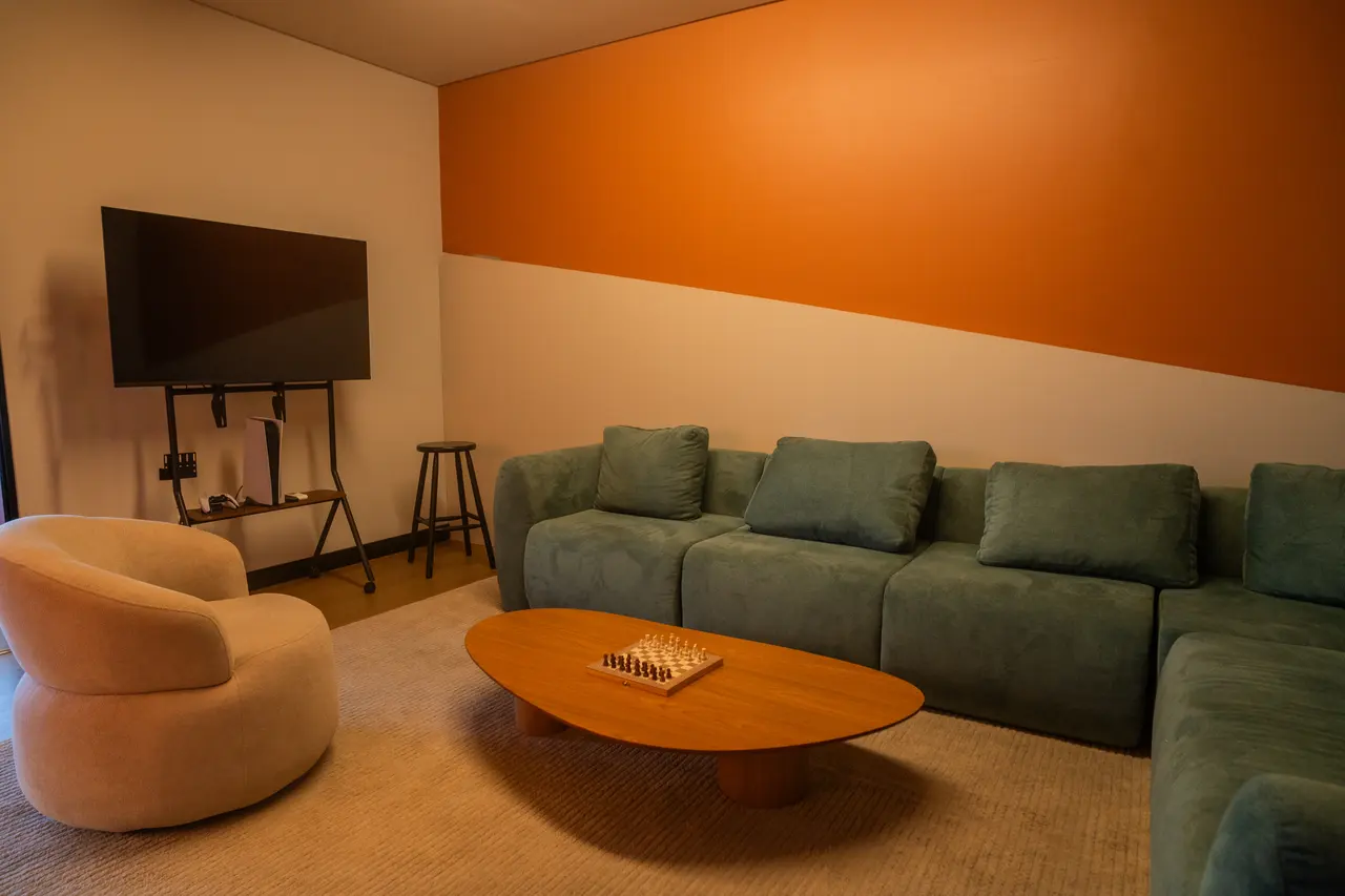 Sala de convivência com sofá, poltrona, TV e uma mesa de centro com tabuleiro de xadrez.